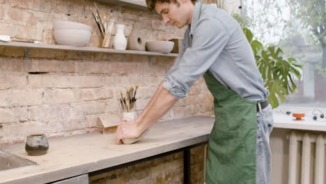 Clerk-In-Agreen-Apron-Kneading-Clay-On-Top-Of-A-Table-In-A-Pottery-Workshop