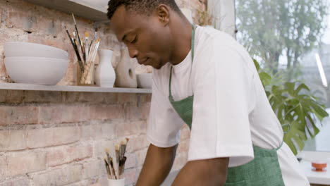 Close-Up-View-Of-American-Clerk-In-Agreen-Apron-Kneading-Clay-On-Top-Of-A-Table-In-A-Pottery-Workshop