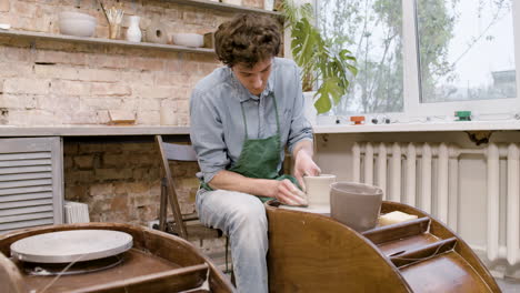 Angestellter-In-Grüner-Schürze,-Der-In-Einer-Werkstatt-Ein-Keramikstück-Auf-Einer-Töpferscheibe-Modelliert