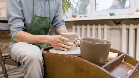 Close-Up-View-Of-Clerk-In-Green-Apron-Modeling-Ceramic-Piece-On-A-Potter-Wheel-In-A-Workshop