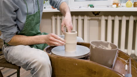 Close-Up-View-Of-Clerk-In-Green-Apron-Modeling-Ceramic-Piece-On-A-Potter-Wheel-In-A-Workshop-1