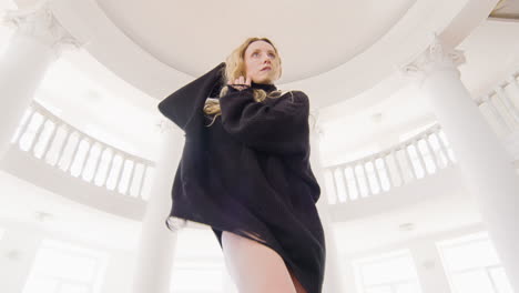 Below-View-Of-A-Focused-Blonde-Woman-In-Black-Long-Sleeve-Loose-Pullover-And-Boots-Performing-A-Contemporary-Dance-In-The-Studio