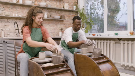 Employees-Wearing-Green-Apron-Modeling-Ceramic-Pieces-On-Potter-Wheel-In-A-Workshop-While-Talking-To-Each-Other