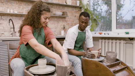 Employees-Wearing-Green-Apron-Modeling-Ceramic-Pieces-On-Potter-Wheel-In-A-Workshop-While-Talking-To-Each-Other-2