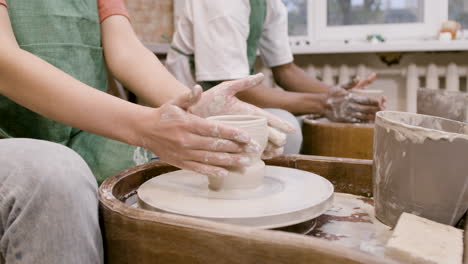 Hände-Von-Mitarbeitern-Mit-Grüner-Schürze,-Die-In-Einer-Werkstatt-Keramikstücke-Auf-Der-Töpferscheibe-Modellieren