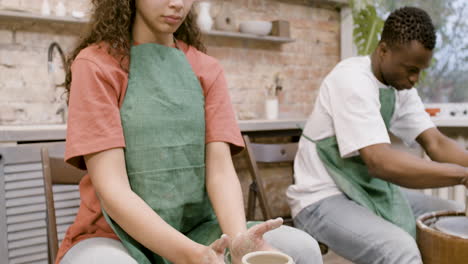 Employees-Wearing-Green-Apron-Modeling-Ceramic-Pieces-On-Potter-Wheel-In-A-Workshop-1