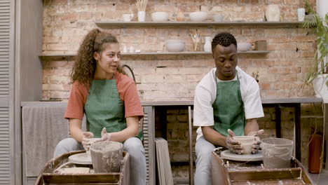 Front-View-Of-Employees-Wearing-Green-Apron-Modeling-Ceramic-Pieces-On-Potter-Wheel-In-A-Workshop-While-Talking-To-Each-Other-1