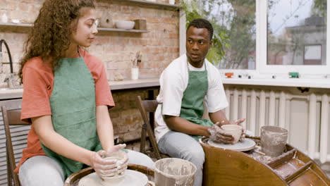 Employees-Wearing-Green-Apron-Modeling-Ceramic-Pieces-On-Potter-Wheel-In-A-Workshop-While-Talking-To-Each-Other-3