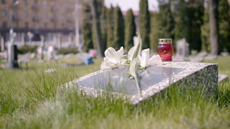 Tombstone-With-A-White-Flower-And-A-Grave-Candle-In-A-Graveyard-On-A-Sunny-Day-1