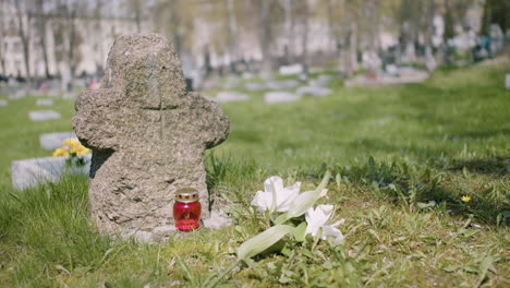 Cross-Tombstone-With-A-White-Flower-And-A-Grave-Candle-On-The-Grass-In-A-Graveyard-On-A-Sunny-Day-1