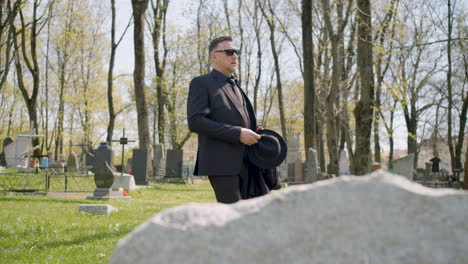 Sad-Man-In-Black-Suit-And-Sunglasses-Walking-In-A-Graveyard-In-A-Sunny-Morning