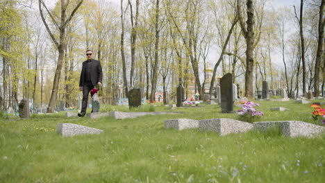 Sad-Man-In-Black-Suit-Holding-Red-Roses-And-Walking-In-A-Graveyard