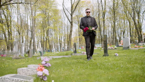 Sad-Man-In-Black-Suit-Holding-Red-Roses-And-Walking-In-A-Graveyard-1