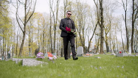 Sad-Man-In-Black-Suit-Holding-Red-Roses-And-Walking-In-A-Graveyard-2