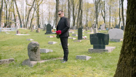 Man-In-Black-Suit-Holding-Red-Roses-Standing-In-Front-Of-A-Grave-In-A-Graveyard-1
