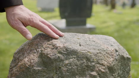 Close-Up-View-Of-Man-Hand-Touching-A-Tombstone-In-A-Graveyard