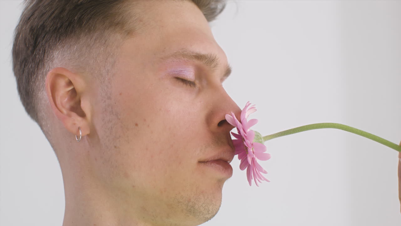 Premium stock video - Handsome young man with earring smelling a flower