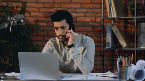 Hombre-De-Negocios-árabe-Hablando-Por-Teléfono-Durante-El-Trabajo-Sentado-En-El-Escritorio-Con-Una-Computadora-Portátil-En-La-Oficina