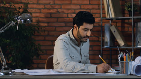 Young-Arabian-Architect-Working-Over-Some-Drawings-For-A-New-Order-Sitting-At-Desk-In-His-Nice-Office