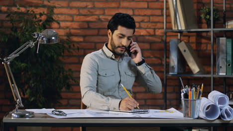 Gut-Aussehender-Arabischer-Geschäftsmann,-Der-Lächelnd-An-Seinem-Schreibtisch-Sitzt-Und-Telefoniert