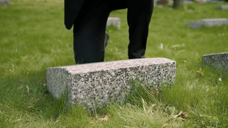 Close-Up-View-Of-Unrecognizable-Man-In-Black-Suit-Cleaning-A-Tombstone-With-A-Handkerchief-In-A-Graveyard