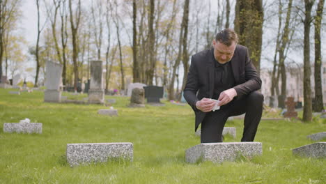 Man-In-Black-Suit-Cleaning-A-Tombstone-With-A-Handkerchief-In-A-Graveyard