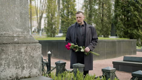 Man-In-Black-Raincoat-And-Suit-Holding-Red-Roses-Standing-In-Front-Of-A-Tombstone-In-A-Graveyard-3