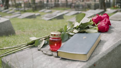 Vista-De-Cerca-De-Rosas-Rojas,-Biblia-Y-Velas-En-Una-Lápida-En-Un-Cementerio