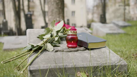 Front-View-Of-Red-Roses,-Bible-And-Candle-On-Tombstone-In-A-Gravevard