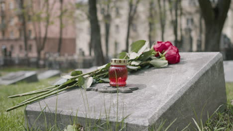 Close-Up-View-Of-Red-Roses-And-A-Candle-On-Tombstone-In-A-Gravevard