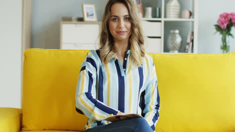 Cheerful-Female-Blogger-Talking-And-Showing-Thumbs-Up-At-Camera-While-Recording-A-Video-For-Her-Followers-Sitting-On-A-Yellow-Sofa-At-Home