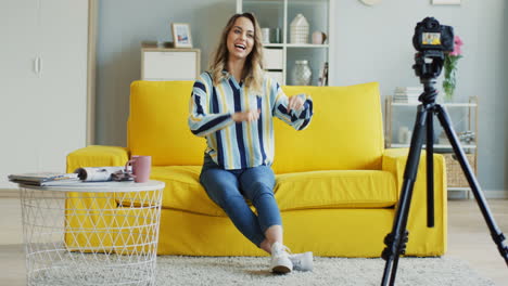 Happy-Female-Blogger-Recording-A-Video-For-Her-Followers-Sitting-On-A-Yellow-Sofa-At-Home
