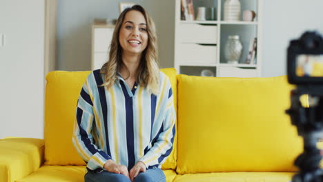 Happy-Female-Blogger-Recording-A-Video-For-Her-Followers-Sitting-On-A-Yellow-Sofa-At-Home-2