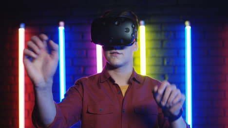 Close-Up-View-Of-Young-Man-In-The-Vr-Glasses-Moving-His-Hands-In-The-Air-In-A-Room-With-Colorful-Neon-Lamps-On-The-Wall