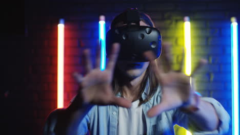 Close-Up-View-Of-Young-Man-In-The-Vr-Glasses-Moving-His-Hands-In-The-Air-In-A-Room-With-Colorful-Neon-Lamps-On-The-Wall-1