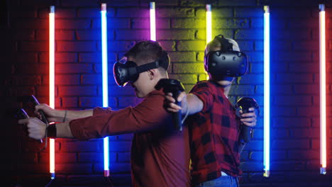 Young-Man-And-Woman-In-Vr-Glasses-And-Using-Joystick-While-Playing-A-Virtual-Reality-Game-In-A-Room-With-Colorful-Neon-Lamps-On-The-Wall