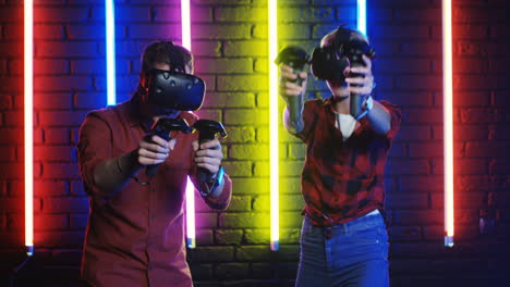 Young-Man-And-Woman-In-Vr-Glasses-And-Using-Joystick-While-Playing-A-Virtual-Reality-Game-In-A-Room-With-Colorful-Neon-Lamps-On-The-Wall-1