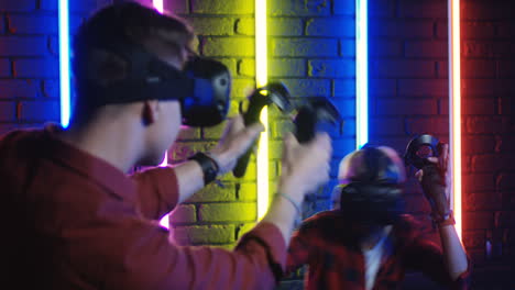 Young-Man-And-Woman-In-Vr-Glasses-And-Using-Joystick-While-Playing-A-Virtual-Reality-Game-In-A-Room-With-Colorful-Neon-Lamps-On-The-Wall-3