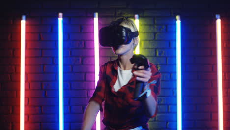 Young-Woman-In-Vr-Glasses-And-Using-Joystick-While-Playing-A-Virtual-Reality-Game-In-A-Room-With-Colorful-Neon-Lamps-On-The-Wall-2