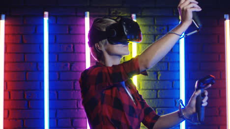 Junge-Frau-Mit-VR-Brille-Und-Joystick-Beim-Spielen-Eines-Virtual-Reality-Spiels-In-Einem-Raum-Mit-Bunten-Neonlampen-An-Der-Wand-4