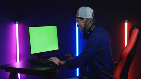 Young-Man-Playing-On-The-Computer-With-Chroma-Key-Screen-In-A-Room-With-Colorful-Neon-Lamps-On-The-Wall