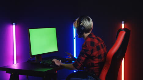 Young-Woman-Playing-On-The-Computer-With-Chroma-Key-Screen-And-Celebrating-A-Victory-In-A-Room-With-Colorful-Neon-Lamps-On-The-Wall