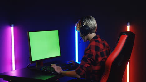 Young-Woman-Playing-On-The-Computer-With-Chroma-Key-Screen-In-A-Room-With-Colorful-Neon-Lamps-On-The-Wall