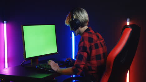 Young-Woman-Playing-On-The-Computer-With-Chroma-Key-Screen-In-A-Room-With-Colorful-Neon-Lamps-On-The-Wall-1