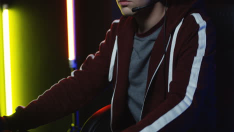 Close-Up-View-Of-Young-Serious-Man-With-Headphones-And-Playing-A-Game-On-The-Computer-In-A-Room-With-Colorful-Neon-Lamps-On-The-Wall-2