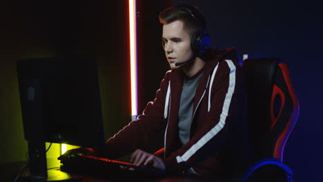 Close-Up-View-Of-Young-Serious-Man-With-Headphones-And-Playing-A-Game-On-The-Computer-In-A-Room-With-Colorful-Neon-Lamps-On-The-Wall-4