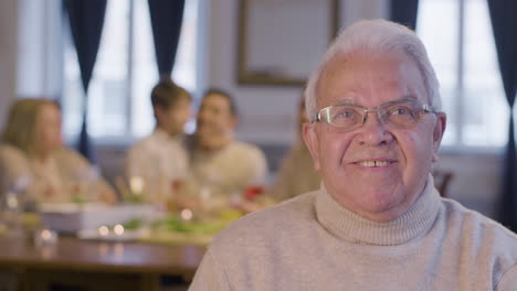 Portrait-Of-A-Senior-White-Haired-Man-In-Glasses-Looking-At-Camera-And-Smiling-While-Spending-Time-With-His-Family-During-A-Party-At-Home