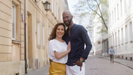 Portrait-Of-A-Happy-Interracial-Couple-Embracing-And-Looking-At-Camera-In-The-Old-Town-Street