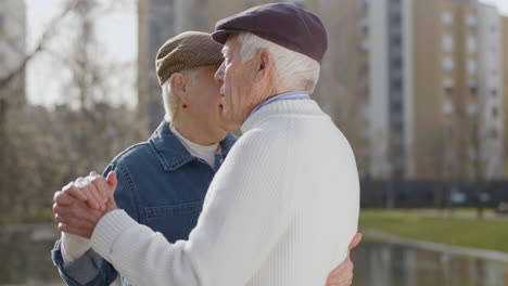 Elderly-Couple-Dancing-In-City-Park-On-Warm-Autumn-Day-With-Multi-Storey-Buildings-In-Background