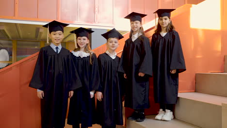 Zoom-In-Of-Happy-Kindergarten-Students-In-Cap-And-Gown-Looking-At-The-Camera-And-Doing-Thumb-Up-Sign-During-The-Preschool-Graduation-Ceremony-1